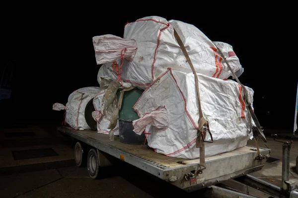 on a car trailer is a large load of white waste bags plastic garbage cans