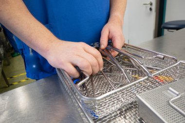 Hastane sterilizasyon departmanının bir çalışanı temizlenmiş aletleri bir konteynıra yerleştirir.