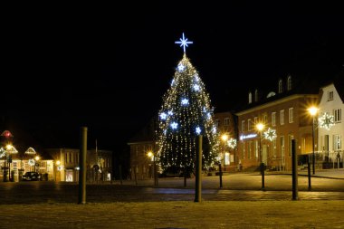 Küçük bir kasabanın pazar yerinde aydınlatılmış bir Noel ağacı duruyor. 