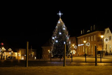 Küçük bir kasabanın pazar yerinde aydınlatılmış bir Noel ağacı duruyor. 