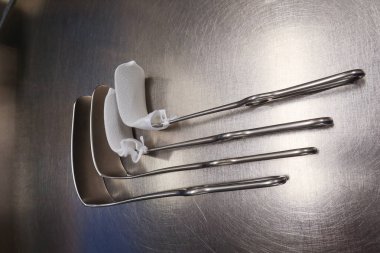 Dört cerrahi abdominal retraktör gümüş bir zeminde yatıyor.