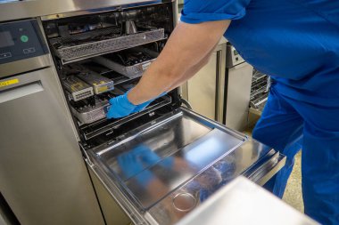 Bir cerrahi departmanının çalışanı bir çamaşır makinesini kullanılmış aletlerle doldurur.