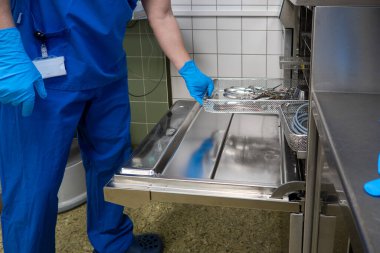Bir cerrahi departmanının çalışanı bir çamaşır makinesini kullanılmış aletlerle doldurur.