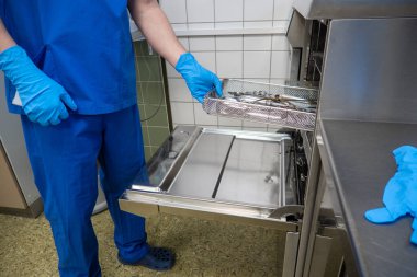 Bir cerrahi departmanının çalışanı bir çamaşır makinesini kullanılmış aletlerle doldurur.