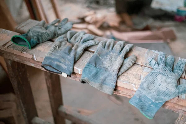 four used, dirty work gloves lying side by side on a wooden board on a construction site