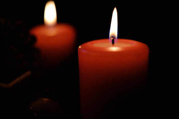 a close up of a burning red candle and the background is dark