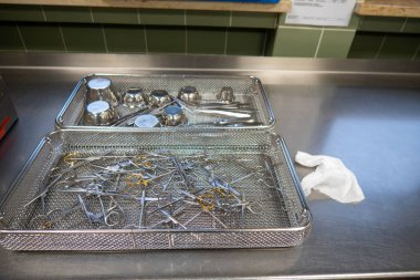 çeşitli cerrahi aletler bir iş yüzeyinde elek içinde yatar.