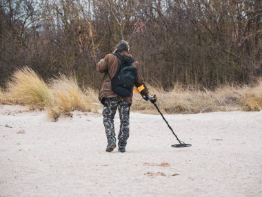 Bir adam plajı metal dedektörüyle arıyor.