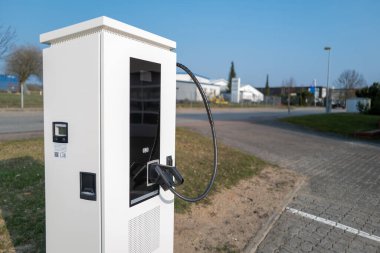 Otoparkta beyaz bir şarj istasyonu var. Elektrikli arabalar.