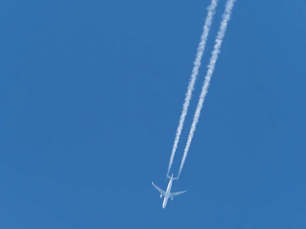 an airplane flies in the blue sky and draws white vapor trails behind it