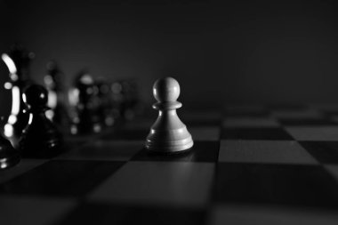 Satranç tahtasındaki siyah taşların önünde beyaz bir piyon yalnız.