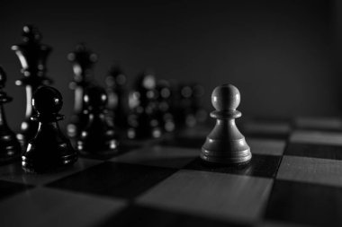 Satranç tahtasındaki siyah taşların önünde beyaz bir piyon yalnız.