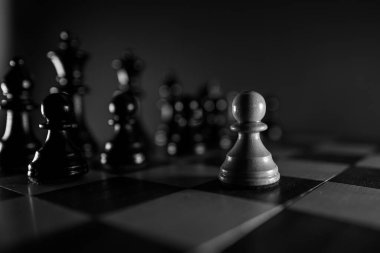 Satranç tahtasındaki siyah taşların önünde beyaz bir piyon yalnız.