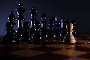 Beyaz piyon satranç tahtasındaki siyah taşların önünde tek başına.