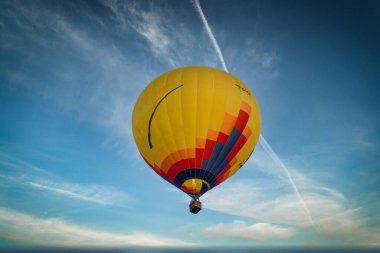 Mavi gökyüzünde uçan sarı bir sıcak hava balonu.
