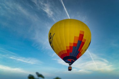 Mavi gökyüzünde uçan sarı bir sıcak hava balonu.