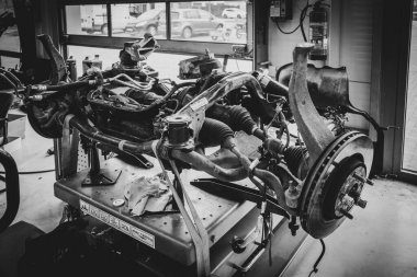 Profesyonel bir oto tamir atölyesinin içinde, süspansiyonlu, direksiyonlu ve direksiyonlu bir arabanın ön çerçevesini gösteren detaylı bir görüntü. Görüntü, araçlar, yangın söndürücü ve geri dönüşümle teknik bir ortam yakalıyor.