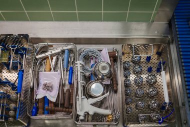 Hastanenin ameliyat odasındaki paslanmaz çelik bir yüzey üzerindeki metal tepsilerde sterilize cerrahi aletlerin tepeden tırnağa görüntüsü. Görüntü ortopedik ve cerrahi aletleri gösteriyor. Tıbbi bir prosedür için hazırlanıyor. Hassasiyeti vurguluyor.