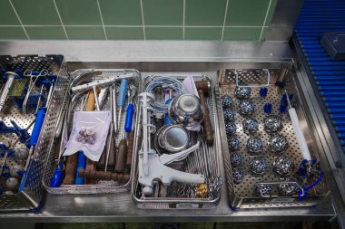 Hastanenin ameliyat odasındaki paslanmaz çelik bir yüzey üzerindeki metal tepsilerde sterilize cerrahi aletlerin tepeden tırnağa görüntüsü. Görüntü ortopedik ve cerrahi aletleri gösteriyor. Tıbbi bir prosedür için hazırlanıyor. Hassasiyeti vurguluyor.