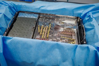 Steril ortopedik alet tepsisinin yüksek çözünürlüklü fotoğrafı. İçinde kemik plakaları, cerrahi vidalar ve hassas aletler var. Travma veya ortopedik ameliyat için hazırlanmış. Metal implant sistemi cerrahi tepsi ve surrou içinde düzenli.