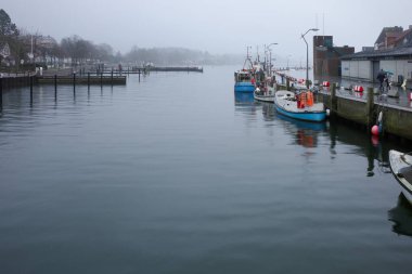 Almanya 'nın Eckernfrde kentindeki liman sahnesinde Baltık Denizi' nin yanındaki bir liman güvertesinde elektrik santralleri görülüyor. Geçici inşaat bariyerleri ve güvenlik ekipmanları ıslak kaldırımda duruyor.