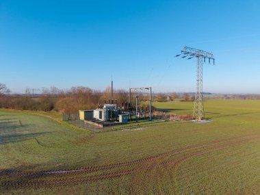 Elektrik santralinin hava aracı görüntüsü ve kırsal bir tarımsal alanda bulunan yüksek voltajlı iletim kulesi. Elektrik hatları yeşil alanlardan geçerek trafo istasyonunu bölgesel elektrik şebekesine bağlıyor. Bu görüntüler...