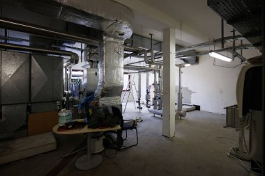 Endüstriyel havalandırma ve havalandırma sistemi ticari ya da endüstriyel bir binanın teknik odasına monte edildi. Görüntü, hava kontrol üniteleri, yalıtılmış hava kanalları, metal havalandırma boruları ve iklim kontrolü için kullanılan mekanik ekipmanları gösteriyor.,