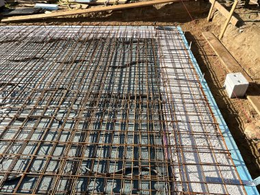 İnşaat alanındaki beton bir temel kaplaması için güçlendirilmiş çelik demirin yakın görüntüsü. Görüntü, izolasyon panelleri üzerine yerleştirilmiş yapısal takviye çubuklarını ve beton dökülmeye hazır formaliteleri gösteriyor. Bu ortak