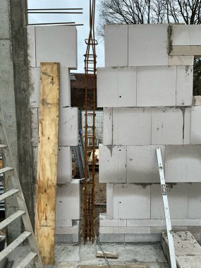 Yapısal bir kolon için beyaz havalandırmalı beton bloklar ve açıkta duran dikey çelik beton takviyeli mason duvar. İnşaat alanı tamamlanmamış saat, beton temel ve merdiveni olan aktif konut inşaatlarını gösteriyor.,