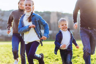Mutlu aile tarlada koşuyor. Baba, anne ve çocuklar yeşil bir tarlada koşuyor..