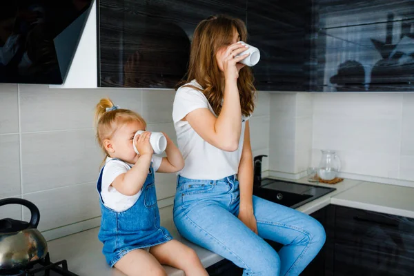 Mãe está bebendo chá na cozinha com sua filhinha. — Fotografia de Stock
