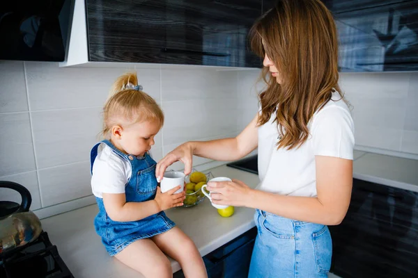 Anya teát iszik a konyhában a kislányával.. — Stock Fotó