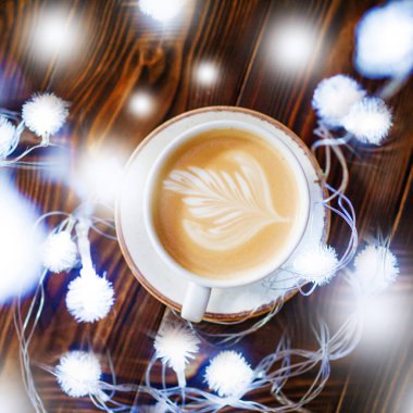 Ahşap arka planda ışıklarla süslenmiş yeni yıl lattesi.