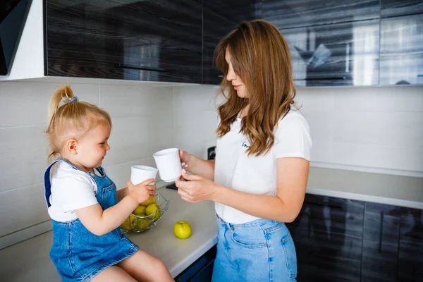 Mãe está bebendo chá na cozinha com sua filhinha. — Fotografia de Stock