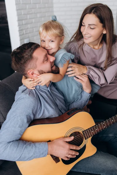 Family plays the guitar. Father plays the guitar for his wife and daughter.