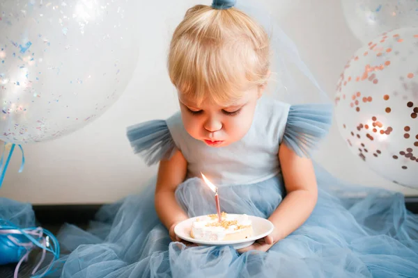 Little blonde girl blows out the candles on the birthday cake.