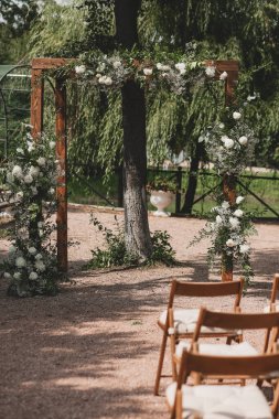 Parkta beyaz çiçeklerle boho tarzında düğün kemeri.