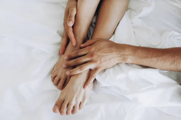 Тонкі гладкі ніжні ноги обіймають руки чоловіка на білих простирадлах . — стокове фото