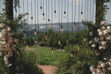 Boho stilinde düğün kemeri Parkta beyaz çiçekler ve ampuller.