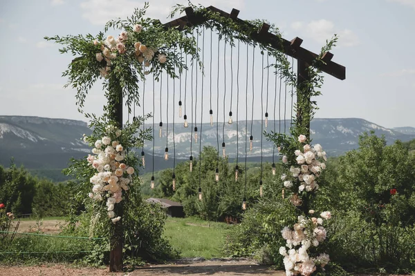 Svatební oblouk na boho stylu s bílými květy v parku se žárovkami. Stock Fotografie