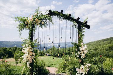 Boho stilinde düğün kemeri Parkta beyaz çiçekler ve ampuller.