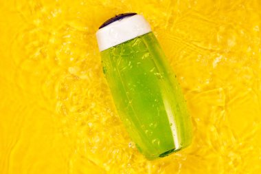 Sarı arka planda yeşil bir şişedeki duş jeli ya da şampuan. Su damlaları ve su damlaları, üst manzara. Vücut ve saç bakımı kavramı, yaz kozmetik ürünleri.