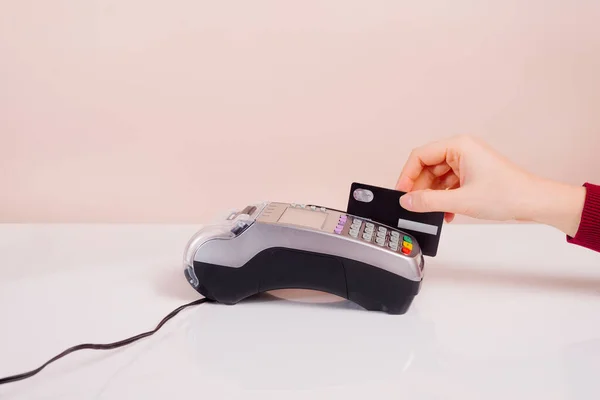 Customer\'s hand near the bar makes payment by credit card by terminal, view of hand device, non-cash method of paying bills in commercial premises concept on pink background.