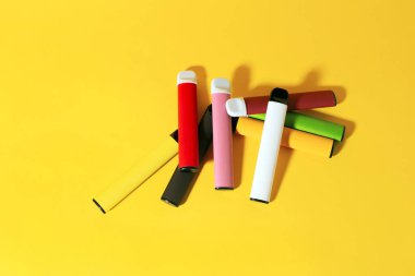 Sarı arka planda gölgeleri olan tek kullanımlık renkli sigaraların yerleşimi. Modern sigara, buhar ve nikotin kavramı. Üst görünüm.