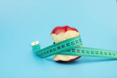 Kırmızı ısırılmış elma ve mavi arkaplanda fotokopi alanı olan mezura.