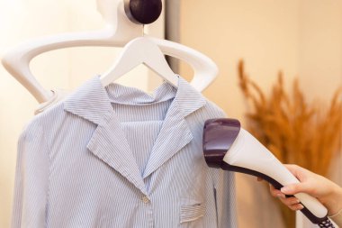 Çamaşır odasında ütü yapmak için buharlı ütü kullanmak. Eldeki pres kıyafetleri için buhar ütüsü yapıyorum. seçici odak.