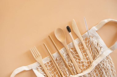 Çevre dostu çanta ve yeşil yaşam için bej arka planda diş fırçası ve sıfır atık kavramı olan bambu çatal bıçak seti. Üst görünüm.