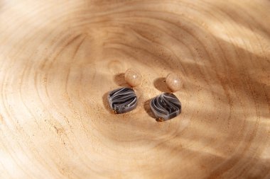 Ahşap bir arka planda el yapımı küpeler. Ahşap. Düz yatıyordu, üst görünüm, güneş ışığının gölgeleriyle minimalist moda mücevherleri.