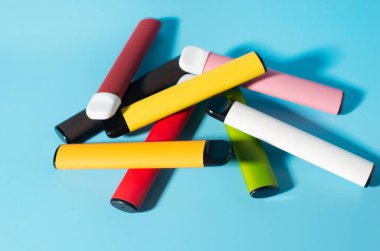 Mavi arka planda gölgeleri olan tek kullanımlık renkli sigaraların yerleşimi. Modern sigara, buhar ve nikotin kavramı. Üst görünüm.