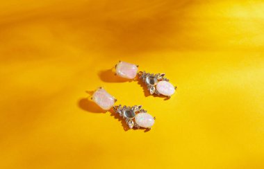 Sarı arka planda el yapımı altın küpeler. Dümdüz uzanmış, manzaralı, güneş ışığının gölgeli minimalist moda mücevherleri.